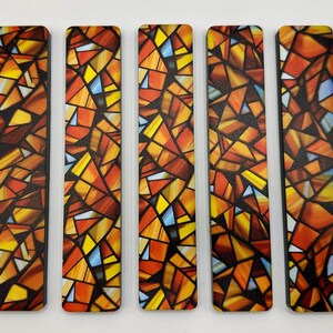 May include: Five rectangular bookmarks with a stained glass design. The design features a mosaic of orange, yellow, and blue geometric shapes. The bookmarks have a black border and a glossy finish.