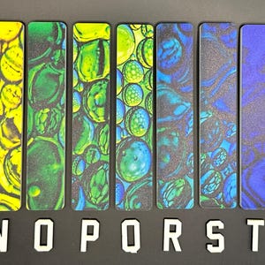 May include: A collection of abstract art bookmarks with vibrant designs. The bookmarks feature a variety of colors, including yellow, green, blue, and black. The letters "M", "N", "O", "P", "R", "S", "T", and "U" are displayed below the bookmarks.