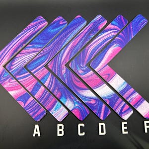 May include: Six angled, L-shaped decorative pieces with a swirling pattern of pink, blue, and purple. The pieces are arranged in a diamond shape, with the letters A through F below them. The background is black.