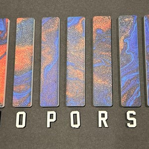 May include: Ten rectangular tiles with a blue and orange marbled pattern and glitter. The tiles are labeled with the letters M, N, O, P, Q, R, S, T, and U.