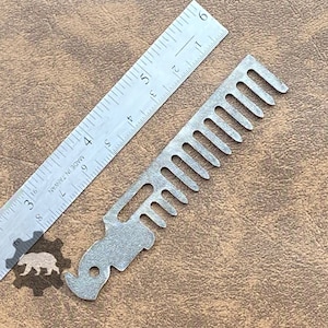 Peut inclure: Un accessoire multifonction pour peigne à barbe argenté avec une règle. Le peigne est à côté d'une règle qui mesure jusqu'à 15 cm. Le texte sur l'image indique "Beard Comb MultiTool Accessory - does not include multitool."