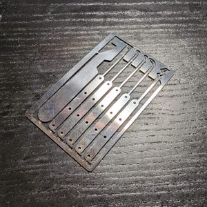 May include: A credit card-sized stainless steel multi-tool featuring a series of integrated lock picking tools. The flat metal card includes five distinct pick profiles and a tension wrench, all laser-cut into the rectangular frame.