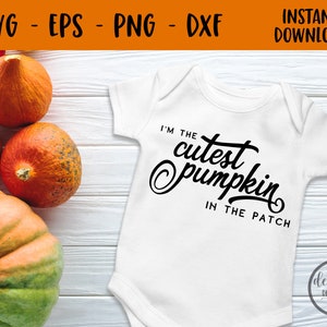 以下が含まれることがあります： 白いベビーロンパースに、黒い文字で「私はパッチの中で一番かわいいカボチャです」と書かれています。ロンパースは、オレンジ色のカボチャがいくつか置かれた白い木製の表面の上に置かれています。