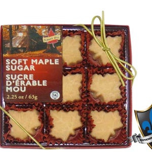 May include: A box of soft maple sugar candies shaped like maple leaves. The candies are in red paper cups and tied with a gold ribbon. The box has the text "SOFT MAPLE SUGAR" and "SUCRE D'ERABLE MOU". The package is 63g.