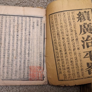 May include: An old, yellowed book with black Chinese characters on the cover. The title of the book is "穎廣治平署".