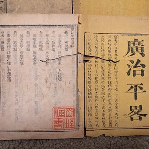 May include: A close-up of a vintage book with a worn, yellowed cover. The title "廣治平器目" is printed in black ink on the cover. The book appears to be a historical text or document.