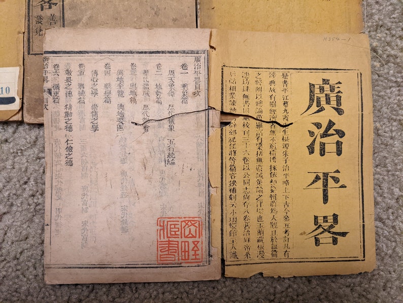 May include: A close-up of a vintage book with a worn, yellowed cover. The title "廣治平器目" is printed in black ink on the cover. The book appears to be a historical text or document.