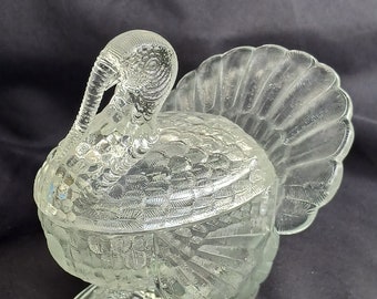May include: A clear glass turkey shaped dish with a detailed design. The turkey has a raised tail and a detailed head and body.