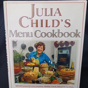 May include: A cookbook titled "Julia Child's Menu Cookbook" with a photo of Julia Child. The cover features text in a burgundy font. The image shows a variety of prepared dishes, including pies, fruits, and a roast, suggesting a focus on diverse recipes.
