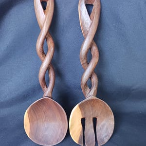 May include: A pair of dark brown wooden salad servers featuring twisted handles with an open triangular cutout at the top. One server is a solid round spoon, while the other is a slotted spoon with two vertical openings in the bowl section.