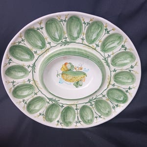 May include: White ceramic serving platter with a central bowl. The platter features a green and white painted design of oval shapes and floral accents. The central bowl has a yellow and green painted design. The platter is likely for serving eggs.