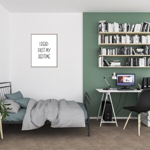 May include: A bedroom with a black metal bed frame, a white nightstand, and a white desk with a black chair. The wall behind the desk is painted a light green color and has a set of white shelves filled with books. The wall behind the bed is white and has a framed print with the text "I read past my bedtime".