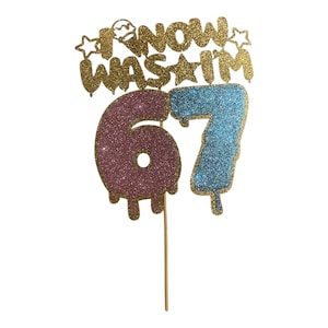 Puede incluir: Adorno para tarta dorado con purpurina con las palabras "I know was I'm" sobre los números "67". El número "6" es rosa y el número "7" es azul. El adorno está fijado a un palito de madera.