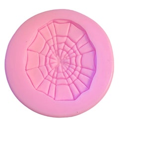 May include: A pink silicone mold shaped like a spider web. The mold is circular and has a raised design of a spider web.
