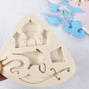 May include: A beige silicone mold with a design of a mosque, a genie lamp, a sword, and a turban. The mold is used for making cake decorations.