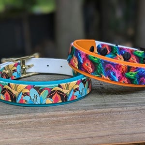May include: Two decorative dog collars. One collar features a floral pattern with blue, yellow, and red flowers on a teal background. The other collar has a dragon pattern with orange trim. Both collars have gold and black hardware.