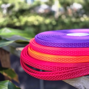 May include: A stack of colorful, coiled rubber strips in shades of red, orange, and purple. Each strip has a textured, dotted surface. The strips are resting on a wooden surface, with a blurred green background.