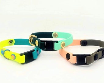 May include: Three colorful pet collars in shades of yellow, teal, green, and peach. Each collar has a black buckle and gold or silver hardware. The collars are made of a flexible material and are designed for pets.