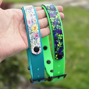 May include: Two silicone wristbands with black snap buttons and metal buckles. One band is teal with a white, pink, and yellow floral pattern. The other band is bright green with a dark purple and green clover leaf pattern on the strap.