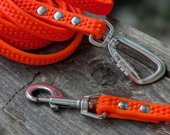 Peut inclure: Laisse orange vif pour chien avec une surface texturée et des fixations en métal argenté. La laisse est enroulée, avec un mousqueton et un crochet pivotant. Conçu pour les propriétaires d'animaux.