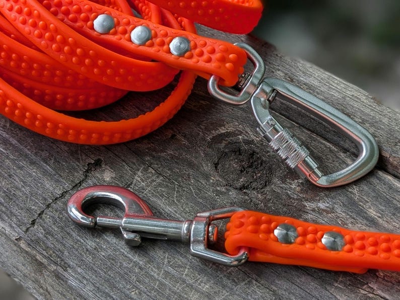 May include: Bright orange dog leash with a textured surface and silver-colored metal hardware. The leash is coiled, with a metal clasp and a swivel hook. The leash is designed for pet owners.