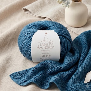 May include: A ball of deep blue yarn with a white paper label featuring the text LAINES du NORD, SILKY WOOL, and a seal illustration. The yarn is textured and soft, accompanied by a matching knitted fabric swatch in the same deep blue colour.