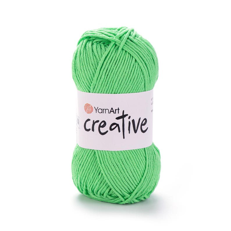 May include: A ball of bright green YarnArt Creative yarn. The yarn is wrapped around itself, with a white label that reads "YarnArt creative" in black script. The yarn is a vibrant, solid colour, perfect for knitting and crochet projects.