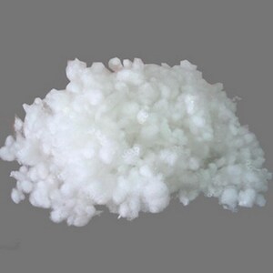 May include: A large pile of fluffy, white polyester fiberfill. The material has a soft, cloud-like appearance and is likely used for stuffing pillows, cushions, or plush toys. The background is a solid, neutral gray.