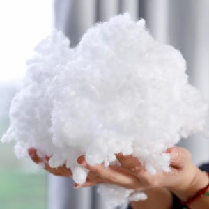 Puede incluir: Una gran nube esponjosa de relleno de fibra de poliéster blanco. El material suave y similar a una nube se sostiene en las manos de una persona. Este relleno se usa a menudo para almohadas, cojines y animales de peluche.