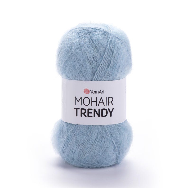 May include: A ball of pale blue mohair yarn with a white label displaying "YarnArt MOHAIR TRENDY". The yarn appears soft and fluffy, suitable for knitting or crochet crafts.