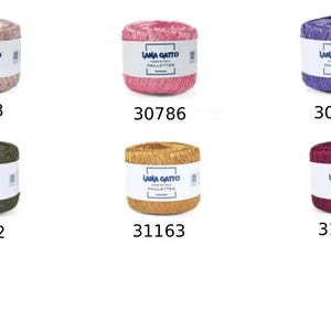 K&ouml;nnte beinhalten: Sechs zylindrische Garnkn&auml;uel von Lana Gatto Paillettes in verschiedenen Farben, darunter Hellrosa, Pink, Lila, Dunkelgr&uuml;n, Gold und Magenta. Jedes Kn&auml;uel hat ein wei&szlig;es Papieretikett mit dem Markennamen und dem Farbcode: 8933, 30786, 30788, 31162, 31163 und 31164.
