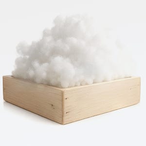 May include: A wooden box filled with a large amount of fluffy, white stuffing. The box is rectangular and made of light-colored wood. The stuffing appears soft and cloud-like, contrasting with the solid wood.