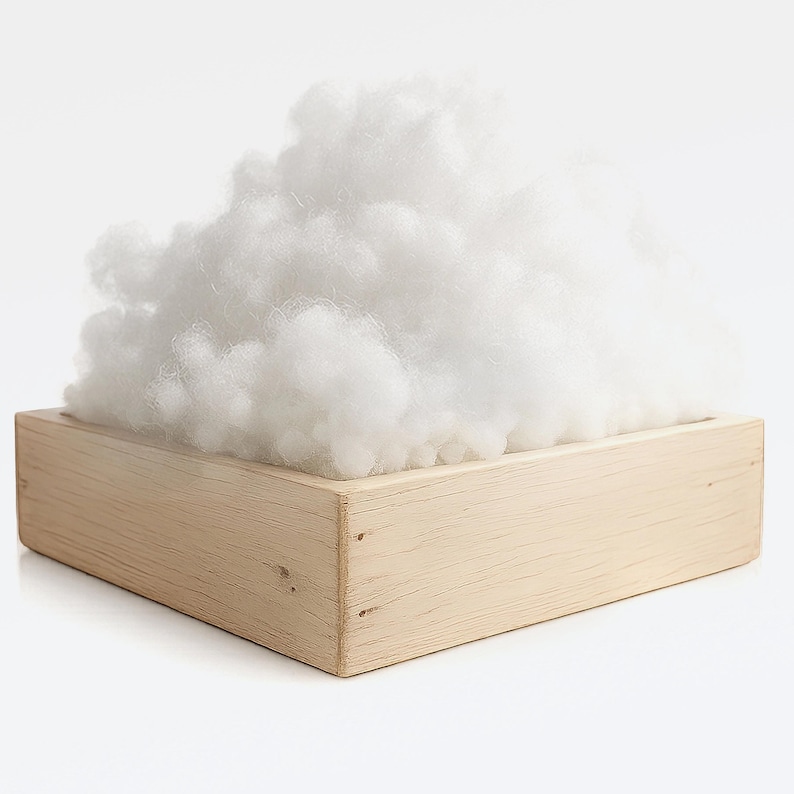 May include: A wooden box filled with a large amount of fluffy, white stuffing. The box is rectangular and made of light-colored wood. The stuffing appears soft and cloud-like, contrasting with the solid wood.