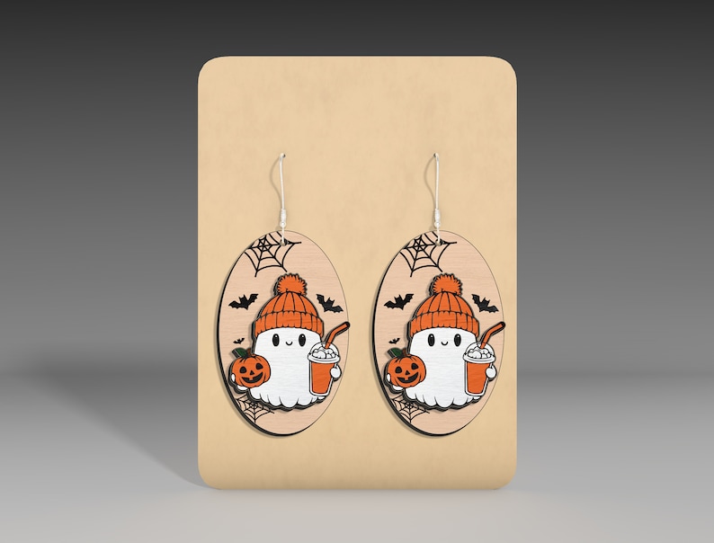 May include: A pair of Halloween-themed earrings featuring a ghost wearing a hat and holding a pumpkin and a drink. The earrings are made of wood and have a brown background with a spiderweb design.
