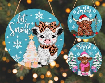 May include: Three round wooden Christmas ornaments with a teal background and the words "Let it Snow". Each ornament features a cartoon cow with festive accessories like a Santa hat, scarf, and bow. Snowflakes and Christmas trees are also included.