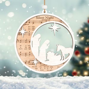 Puede incluir: Adorno navide&ntilde;o de madera blanco con un dise&ntilde;o recortado de la escena de la natividad y la letra de la canci&oacute;n "Noche de Paz".