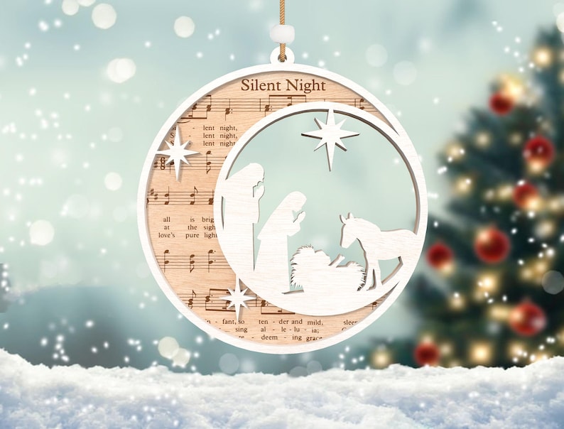 Puede incluir: Adorno navide&ntilde;o de madera blanco con un dise&ntilde;o recortado de la escena de la natividad y la letra de la canci&oacute;n "Noche de Paz".