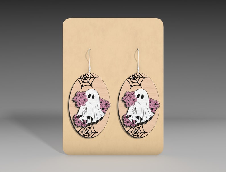 May include: A pair of oval-shaped wooden earrings with a ghost holding pink flowers and a spiderweb design.
