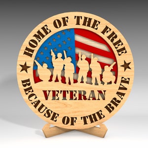 May include: Wooden round sign with an American flag design and the text "Home of the Free Because of the Brave" with the word "Veteran" in the center.