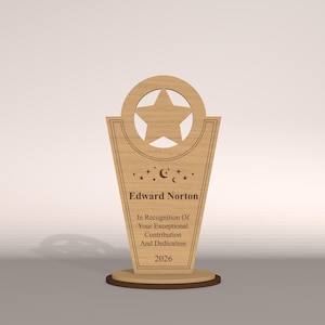 May include: A wooden trophy with a star cutout at the top and a star shape inside. The trophy has the name "Edward Norton" and the text "In Recognition Of Your Exceptional Contribution And Dedication 2026".