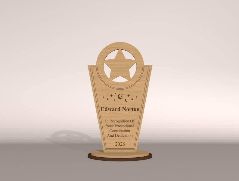 May include: A wooden trophy with a star cutout at the top and a star shape inside. The trophy has the name "Edward Norton" and the text "In Recognition Of Your Exceptional Contribution And Dedication 2026".