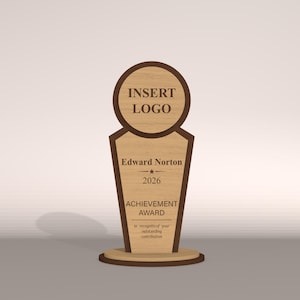 May include: A wooden achievement award with a light brown finish and dark brown trim. The award features a circular top with the text "INSERT LOGO", the name "Edward Norton", the year "2026", and the words "ACHIEVEMENT AWARD".