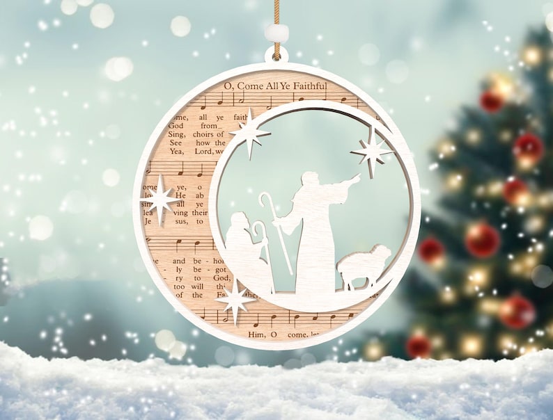 Puede incluir: Un adorno navide&ntilde;o de madera blanco con forma de media luna con una escena de la natividad en su interior. El adorno presenta un pastor, una oveja y una estrella. El adorno est&aacute; decorado con la letra del villancico "O Come All Ye Faithful".