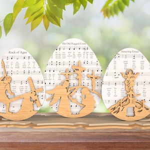 Puede incluir: Tres huevos de Pascua de madera decorados con partituras de himnos y diseños cortados con láser. Los huevos están titulados "Rock of Ages", "The Old Rugged Cross" y "Amazing Grace".