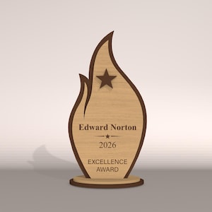 May include: A wooden Excellence Award trophy in a flame shape. The trophy has a light brown center with a dark brown outline and base. The text "Edward Norton", "2026", and "EXCELLENCE AWARD" are engraved on the front, along with a star.