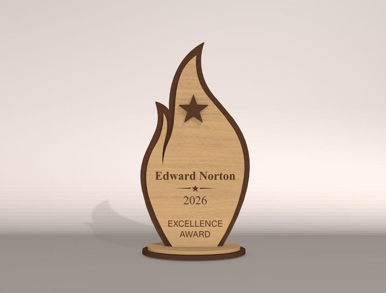 May include: A wooden Excellence Award trophy in a flame shape. The trophy has a light brown center with a dark brown outline and base. The text "Edward Norton", "2026", and "EXCELLENCE AWARD" are engraved on the front, along with a star.