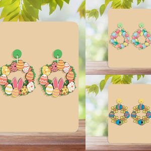May include: Two pairs of colorful Easter egg wreath earrings. One pair features a wreath of pastel colored eggs with a bunny rabbit in the center. The other pair features a wreath of blue, yellow, and green eggs with a yellow flower in the center.
