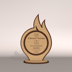 May include: A wooden achievement award with a flame-like design. The award features a circular center with the name "Edward Norton" and the year "2026". The text "ACHIEVEMENT AWARD" is also visible. The award is made of light and dark brown wood.