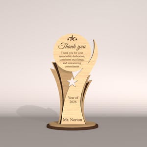 May include: A wooden trophy with a light brown finish. The trophy features the words "Thank you" and a message of appreciation. It includes the year "2026" and the name "Mr. Norton". The design incorporates star shapes and a decorative base.