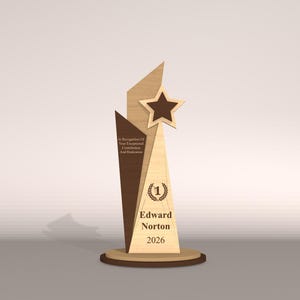 May include: A wooden trophy with a star and geometric design. The trophy has a brown star, a light brown and dark brown body, and a round base. Text on the trophy reads "Edward Norton 2026" and "In Recognition Of Your Exceptional Contribution And Dedication."